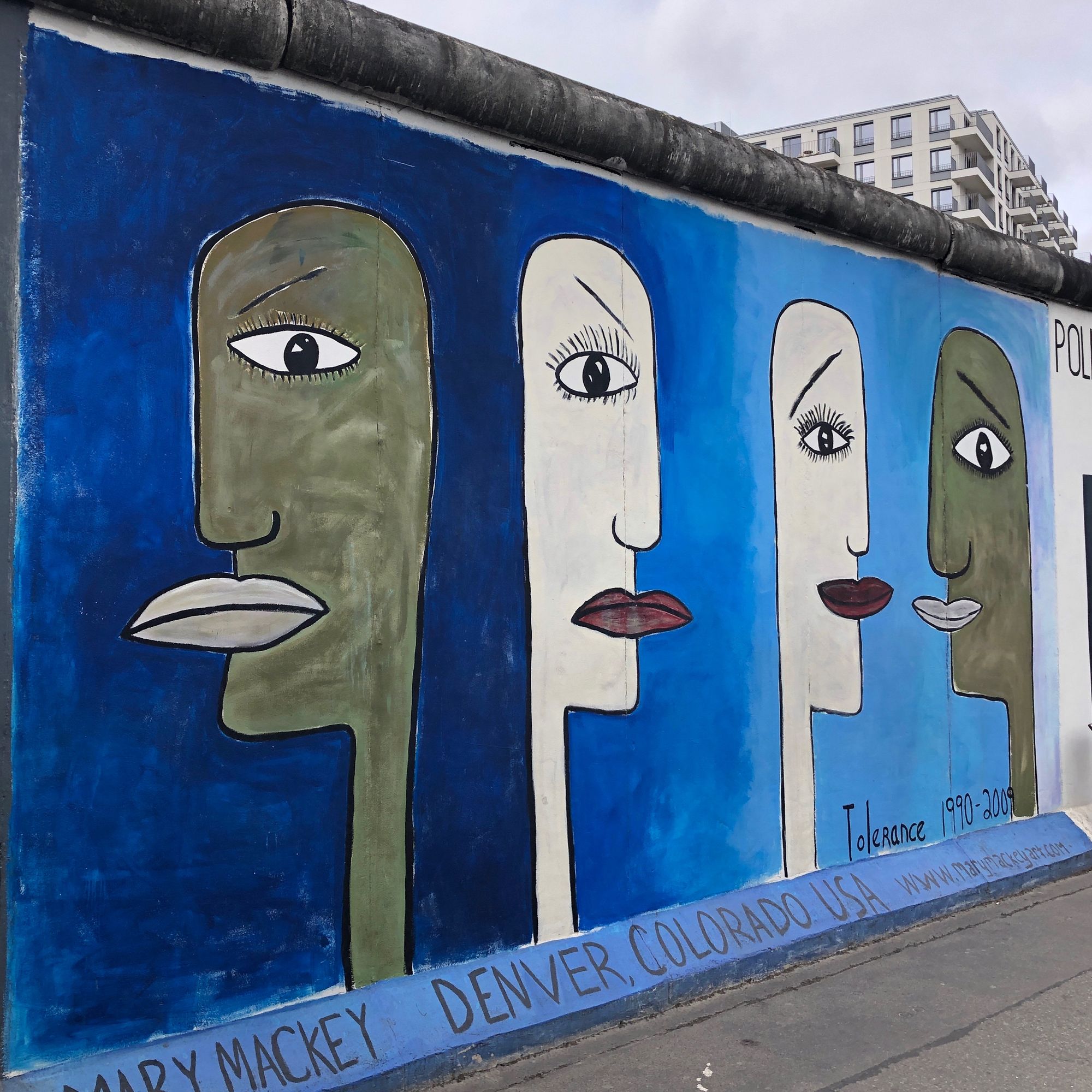 A blue East Side Gallery mural with four elongated faces representing tolerance