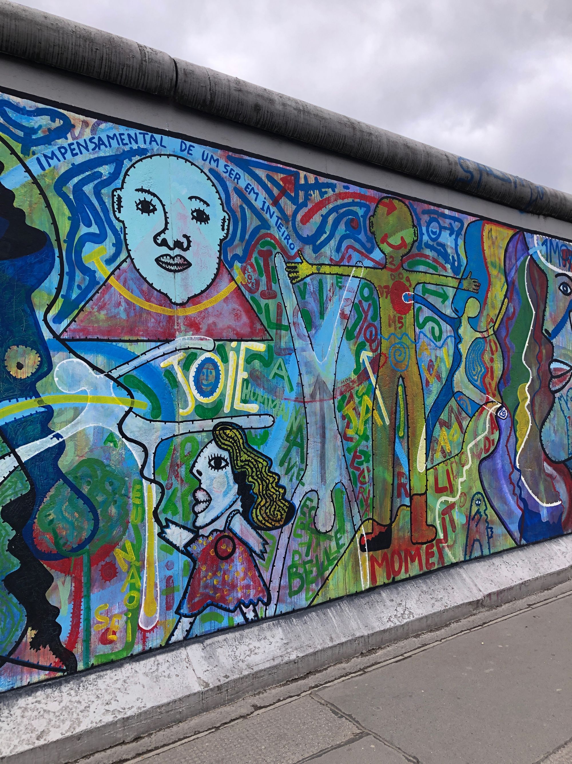 A colorful East Side Gallery mural filled with abstract faces, figures, and overlapping words