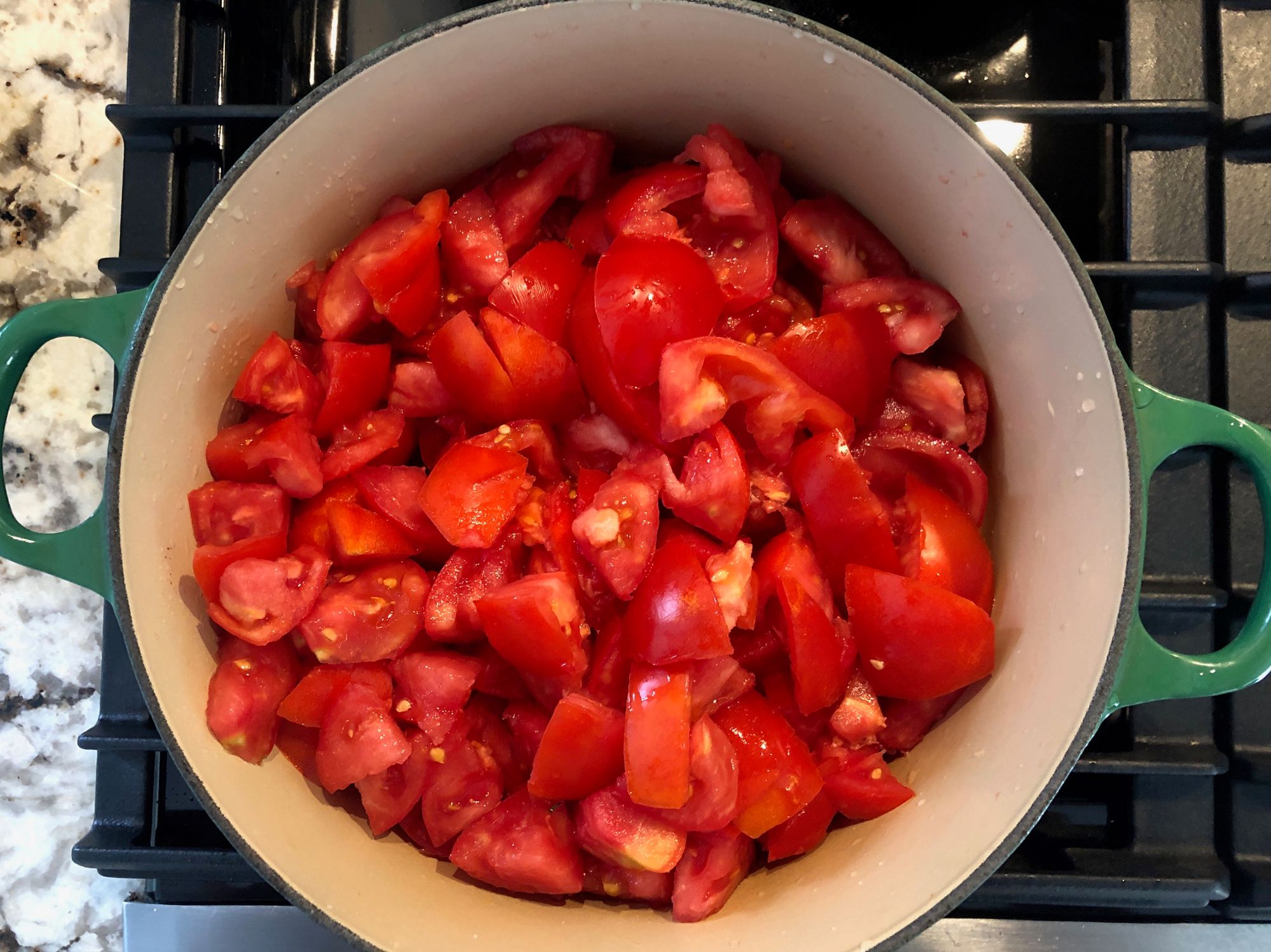 Roughly chopped tomatoes filling a green Dutch oven on the stove