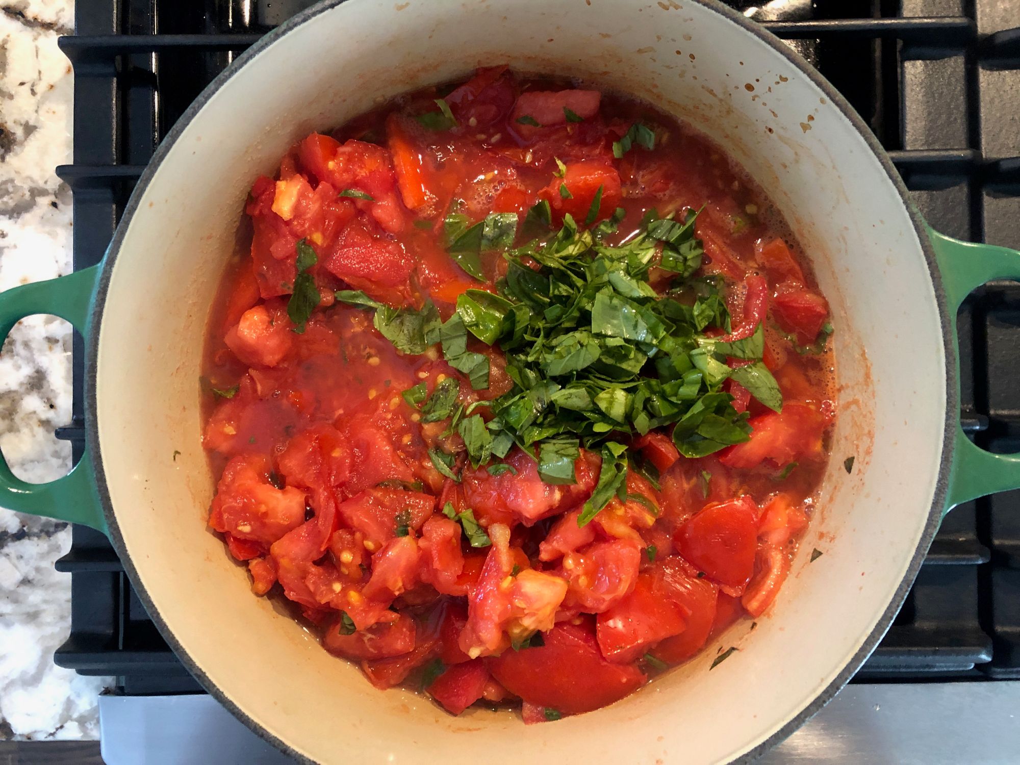 Chopped basil added to tomatoes as they begin cooking