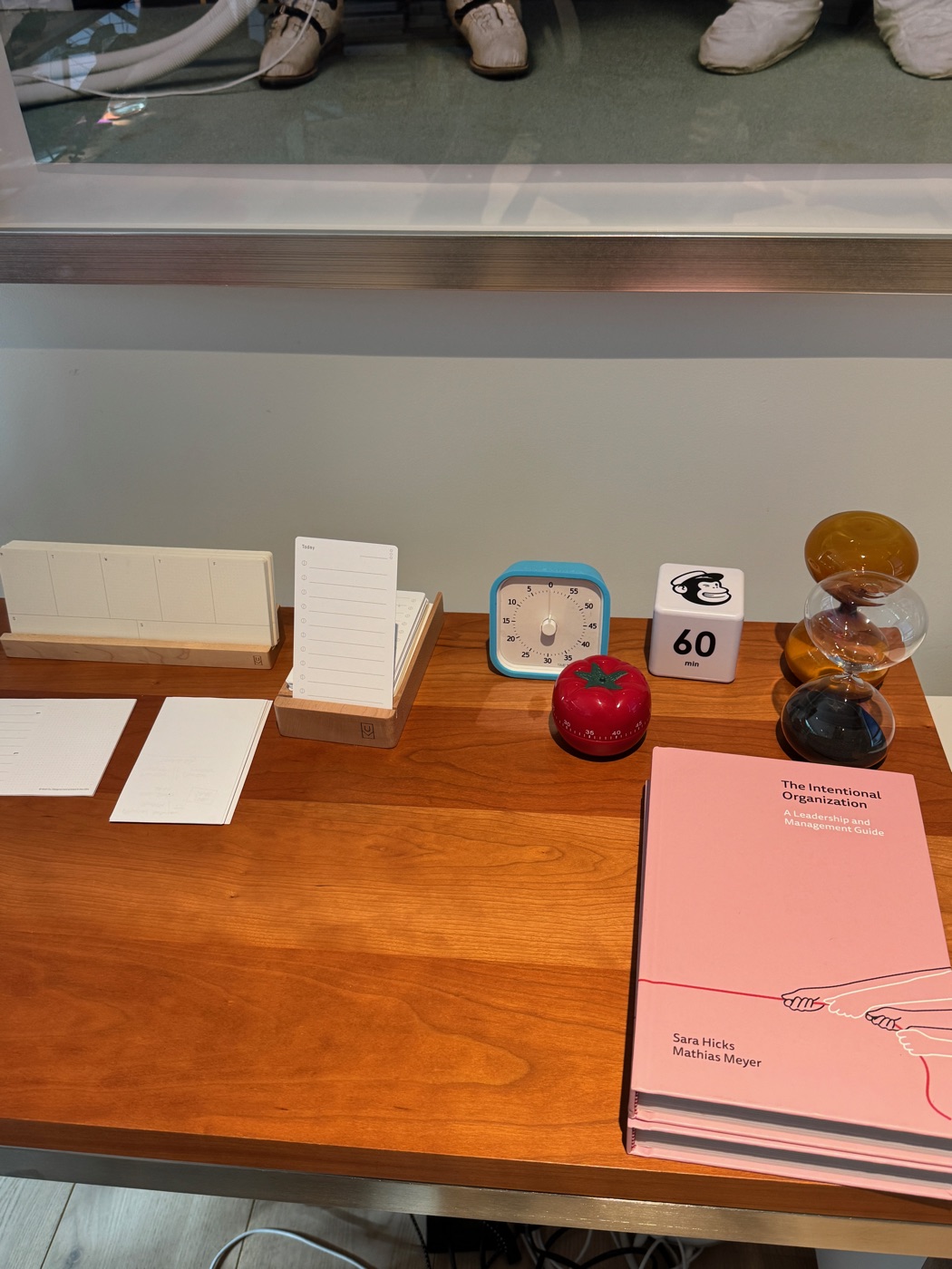 A collection of sand and mechanical timers beside index cards and copies of The Intentional Organization on my wooden desk.