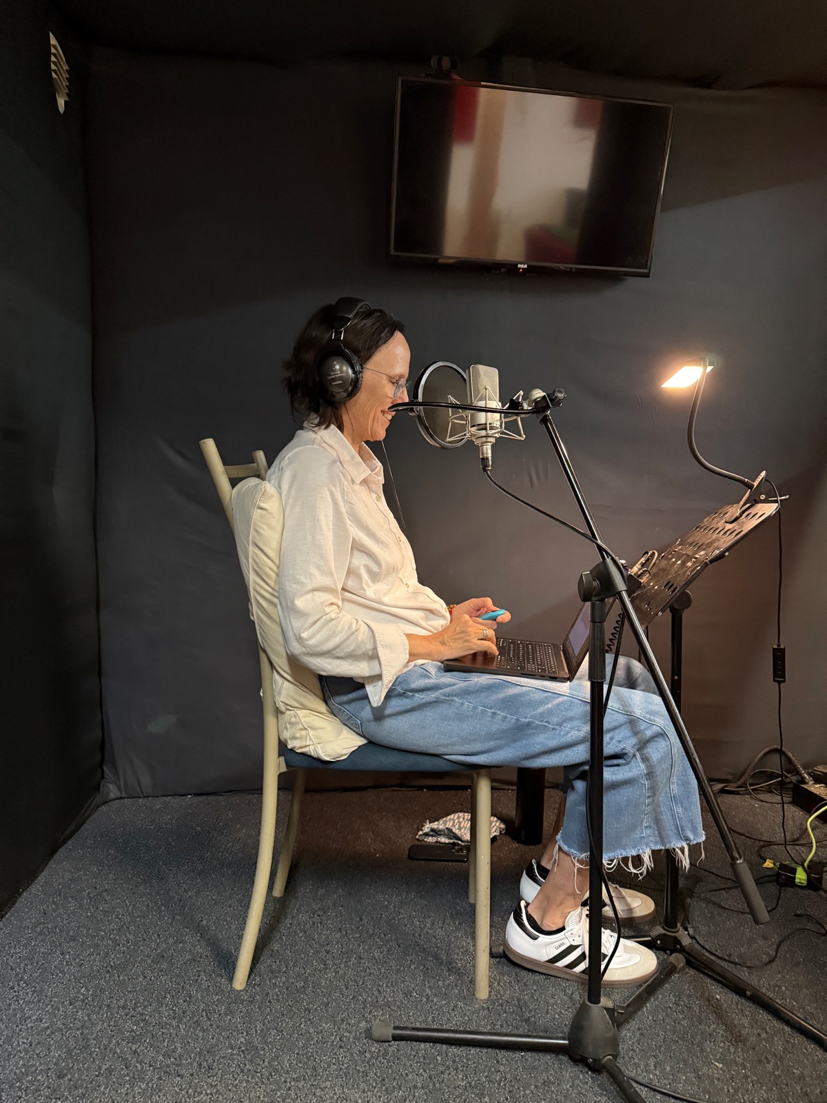 Me wearing headphones and seated at a microphone in the recording booth, with a laptop on my lap.